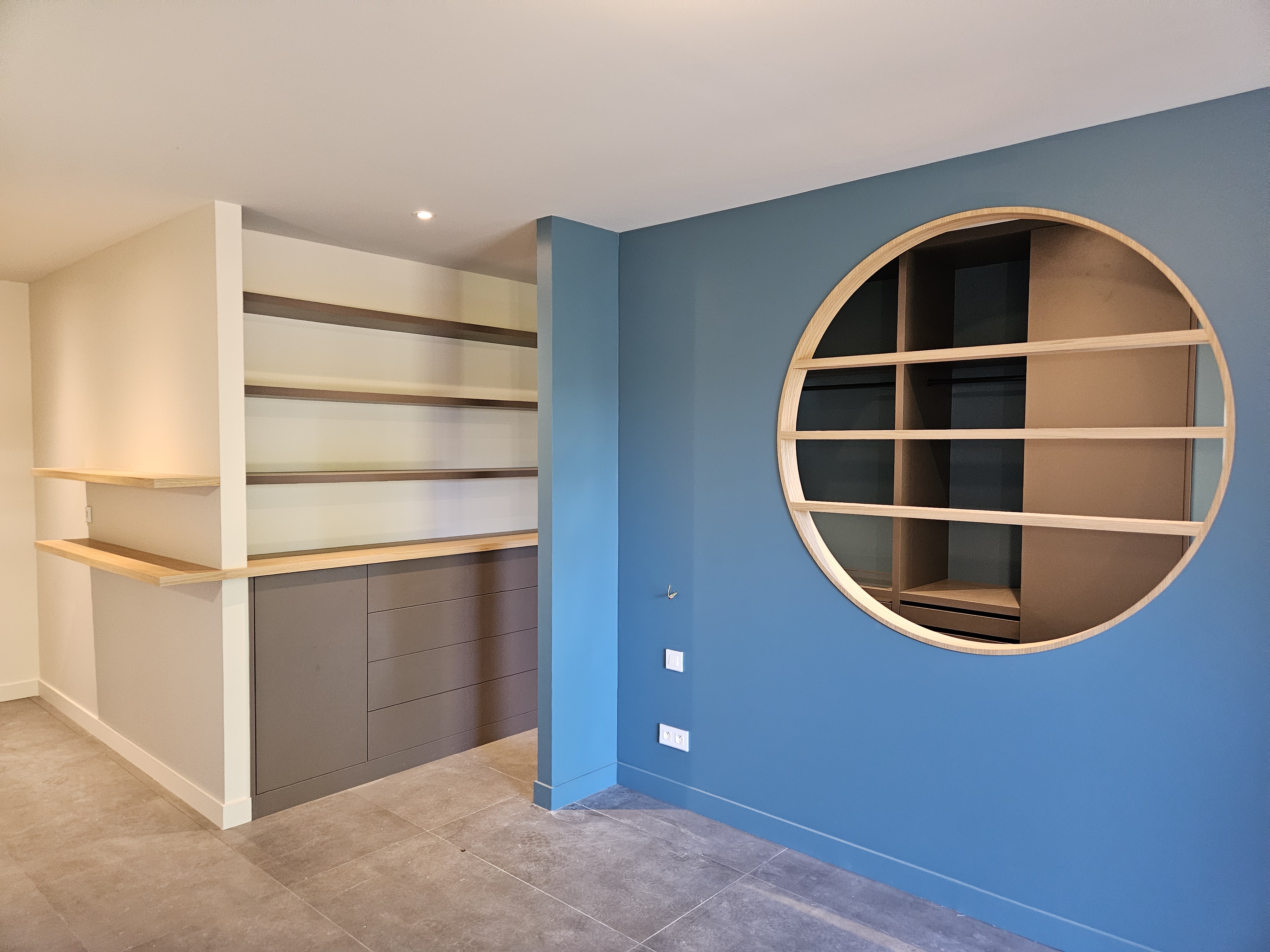 Bibliothèque murale avec rangement bleu et étagères en bois, création sur mesure par MPE Création Bois, expert en menuiserie et agencement à Lyon.